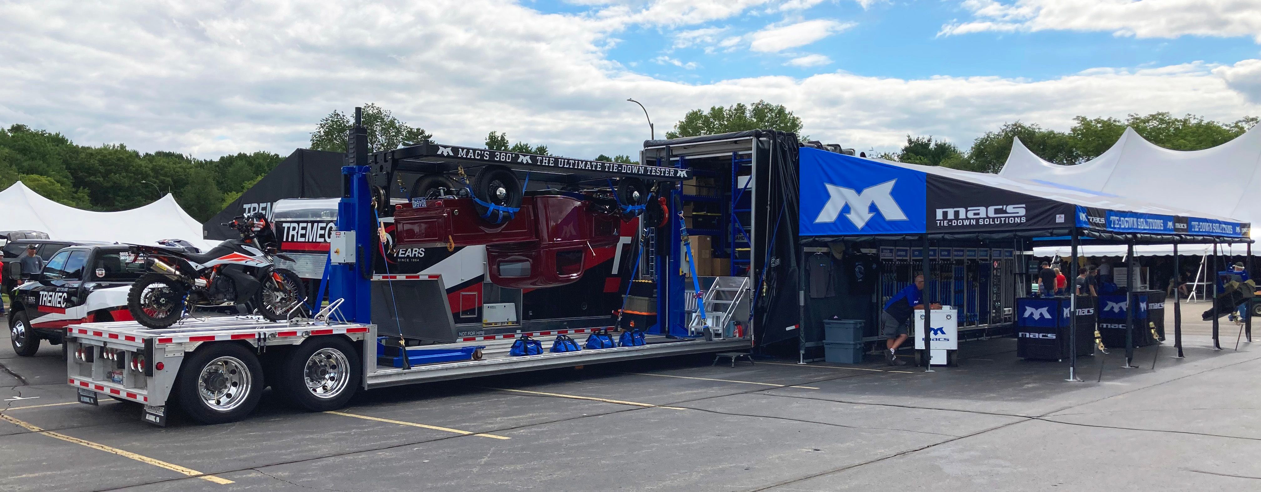 The Mac's Custom Tie-Downs booth at a car show with their rotator truck in the rear.