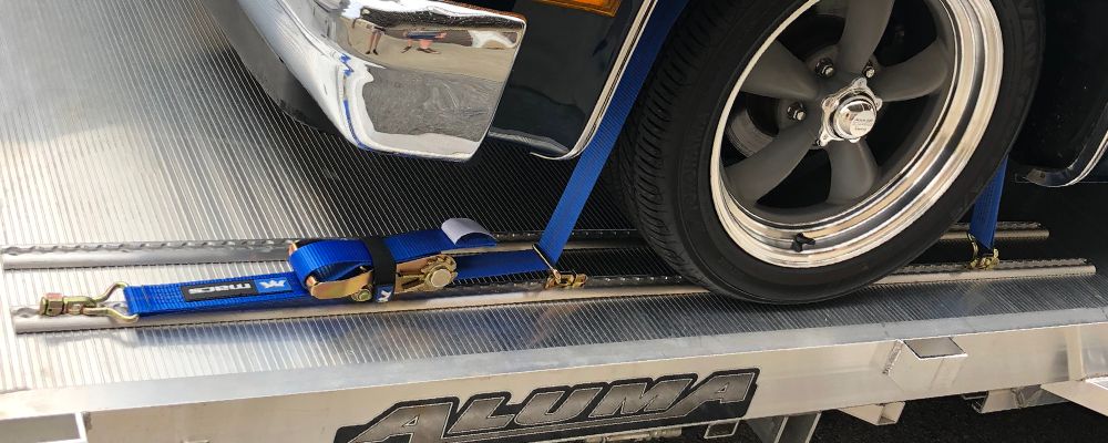 Versatie l-track with blue Mac's straps holding down a vehicle on a trailer